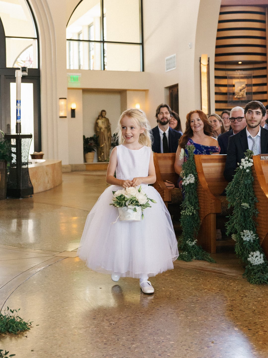 The flower girl walking down the aisle with a basket of white flowers