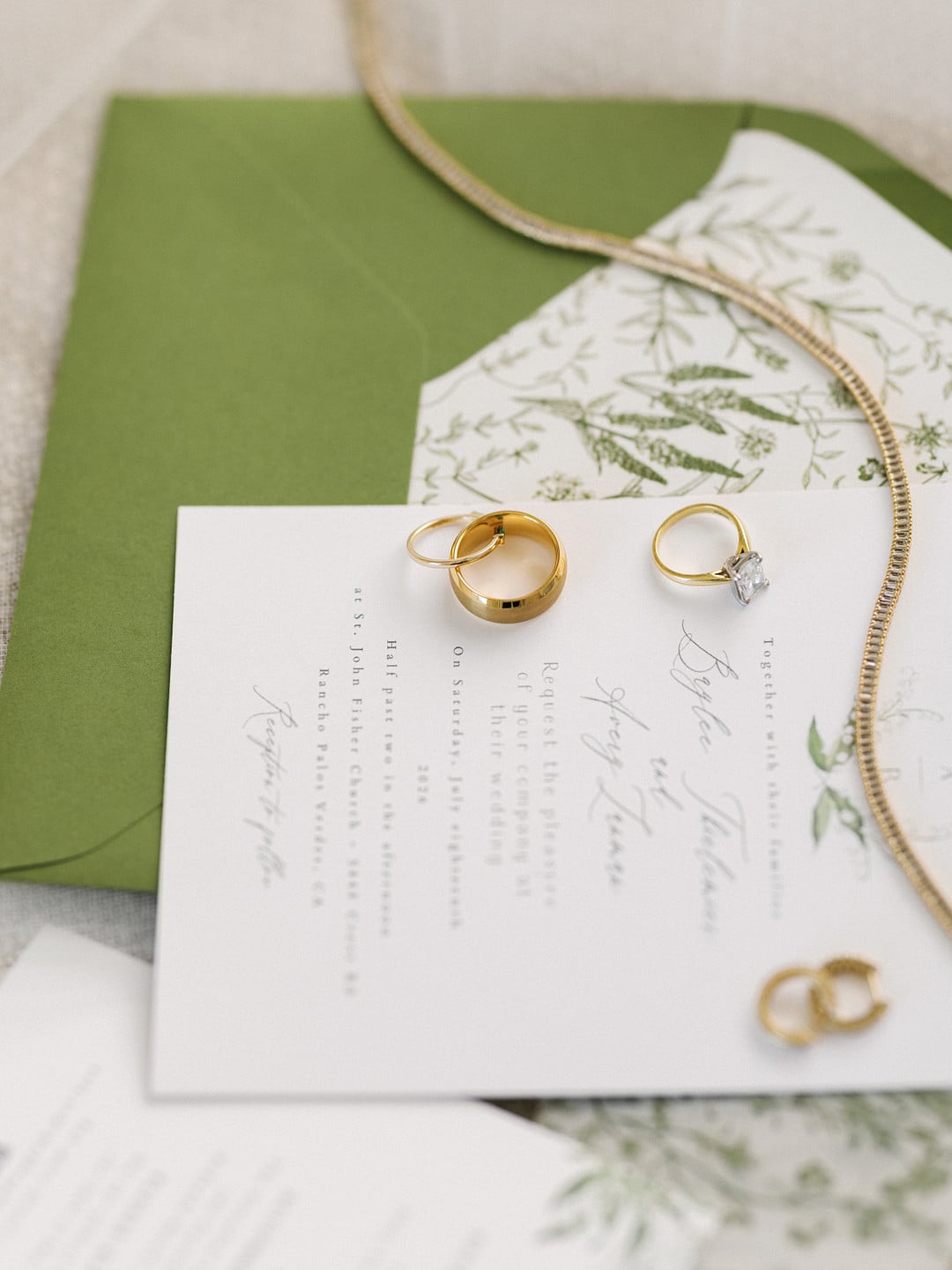 Wedding invitation with green envelope, gold necklace, and the couple's wedding rings