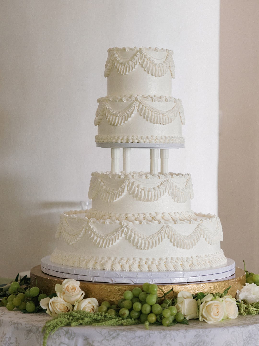 Four-tier Lambeth-style wedding cake with piped swags and columns on a gold stand