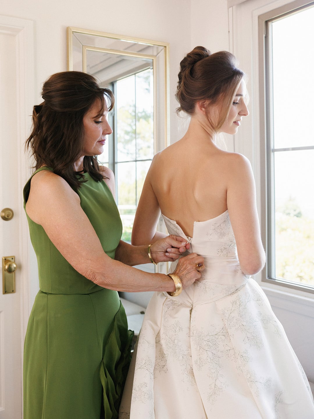 Baylee's mom in a green gown buttoning her into her wedding dress