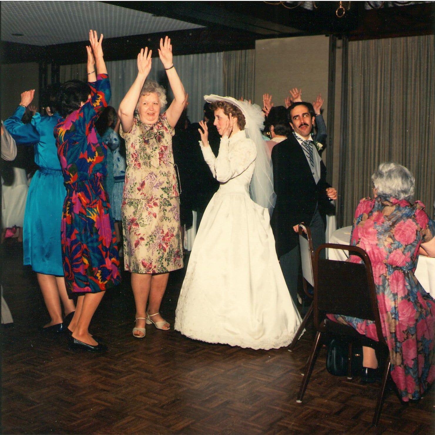 Bride dancing with her arms up in a crowd of guests at a 1988 reception