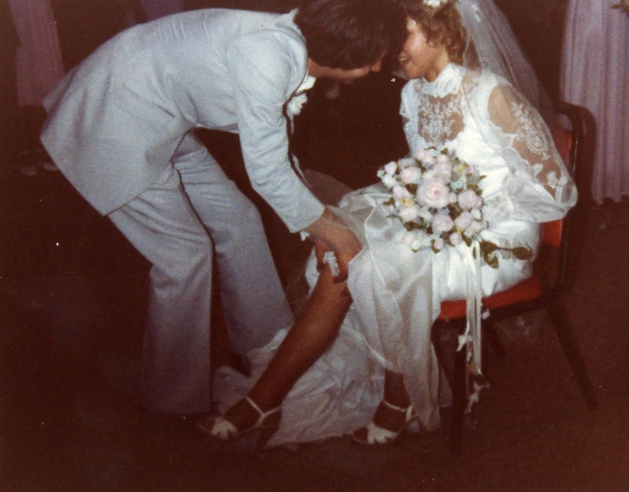 Groom kneeling to remove the garter at a 1982 wedding reception