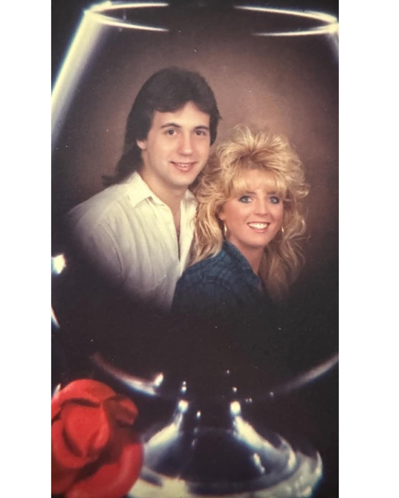 1980s "wine glass photo": a couple with big feathered hair double-exposed inside a giant brandy snifter with a red rose