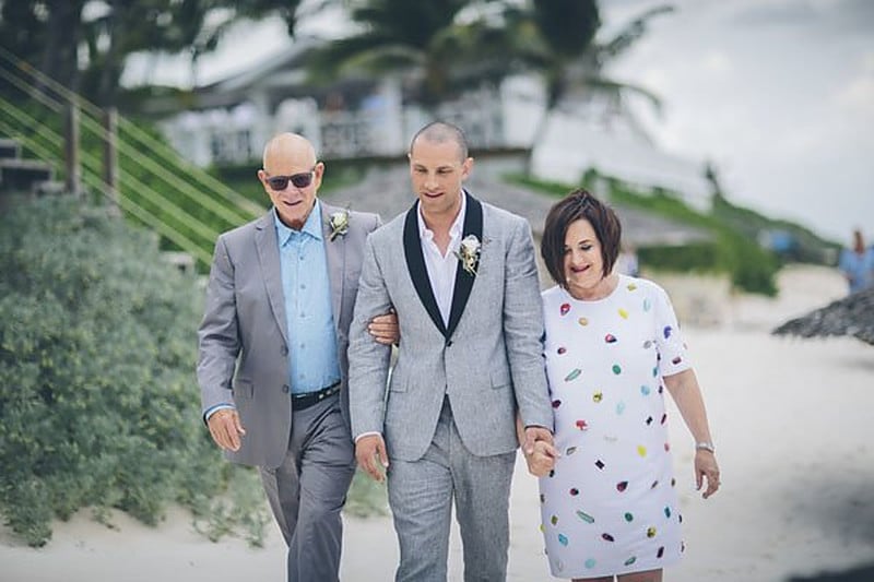 Groom walking a beach aisle with his mother and father on each arm