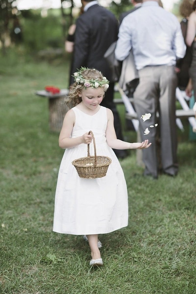 A flower girl in a floral crown tossing petals from a basket as she walks down the aisle