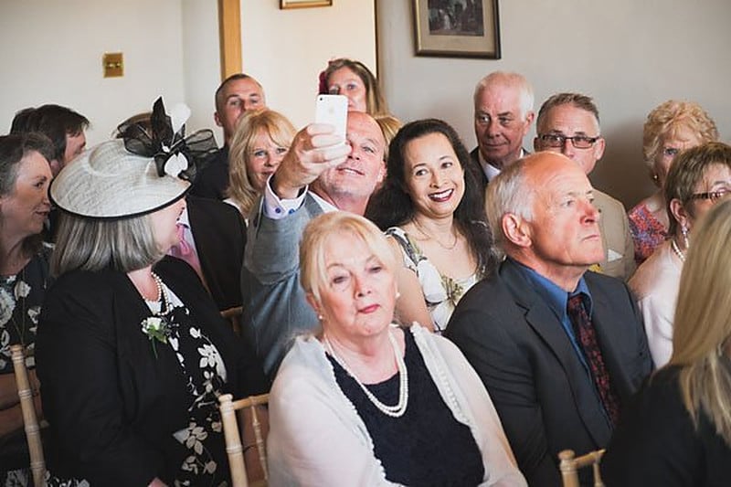 Wedding guests and family seated at an English ceremony, one in a fascinator, watching the couple