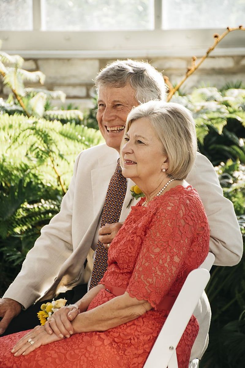 Parents of the couple seated at the ceremony, the mother in a red lace dress, laughing together