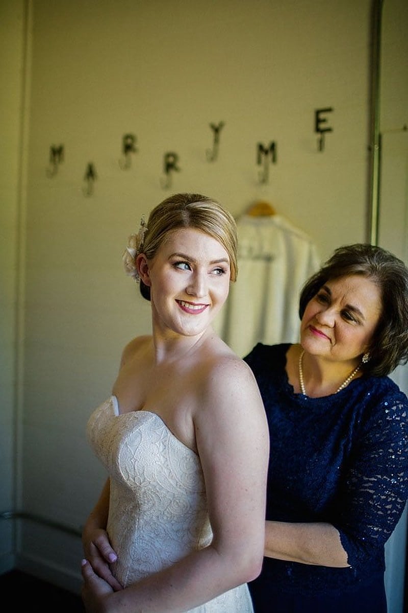 A bride in her gown with her mother in navy lace beside her while getting ready