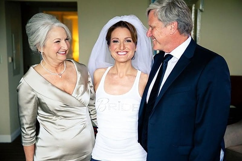 The mother of the bride in a champagne gown smiling with the bride and her father before the ceremony