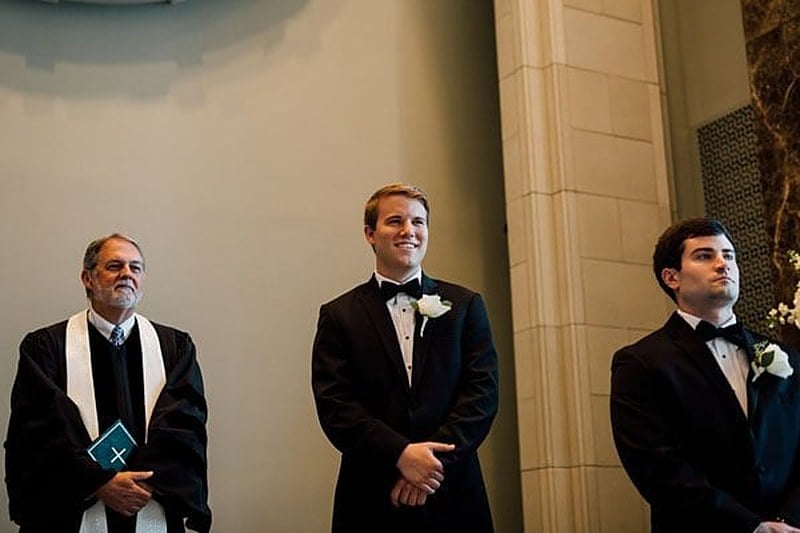 An officiant, the groom and his best man waiting at the front of the church before the processional