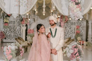 Riya in a blush pink lehenga walking toward Jay at the white carved mandap