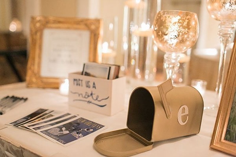 A Post Us a Note card station with a gold mailbox and framed photos at a wedding reception