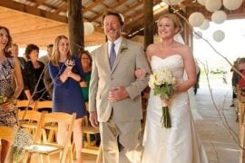 A father walking his daughter down the aisle under paper lanterns at a rustic Louisiana barn wedding
