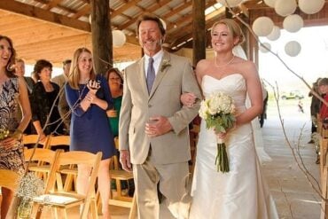 A father walking his daughter down the aisle under paper lanterns at a rustic Louisiana barn wedding