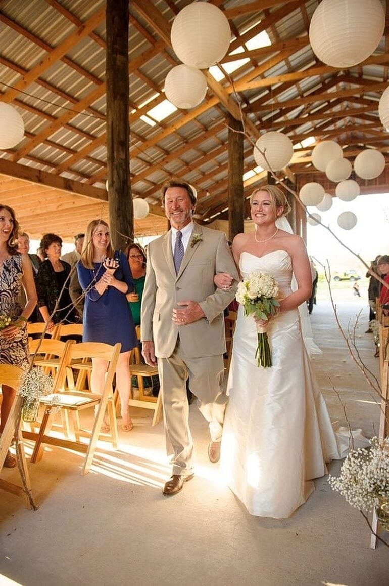 A father walking his daughter down the aisle under paper lanterns at a rustic Louisiana barn wedding