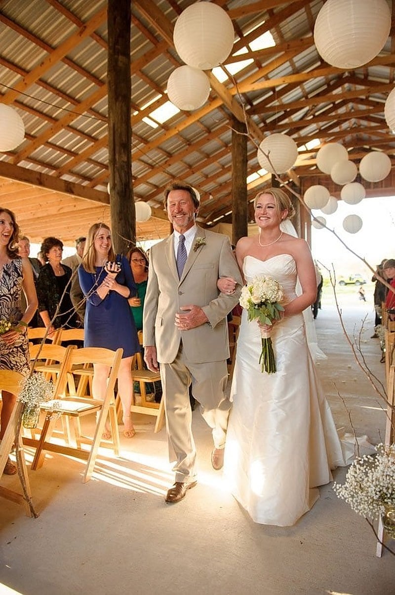 A father walking his daughter down the aisle under paper lanterns at a rustic Louisiana barn wedding