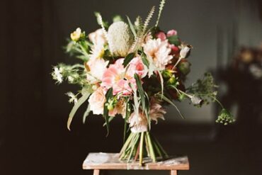 Red, blush and white wedding bouquet with anemones and greenery on a wooden stool