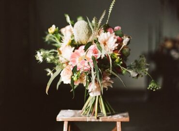 Red, blush and white wedding bouquet with anemones and greenery on a wooden stool