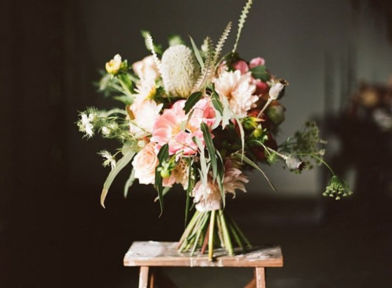 Red, blush and white wedding bouquet with anemones and greenery on a wooden stool
