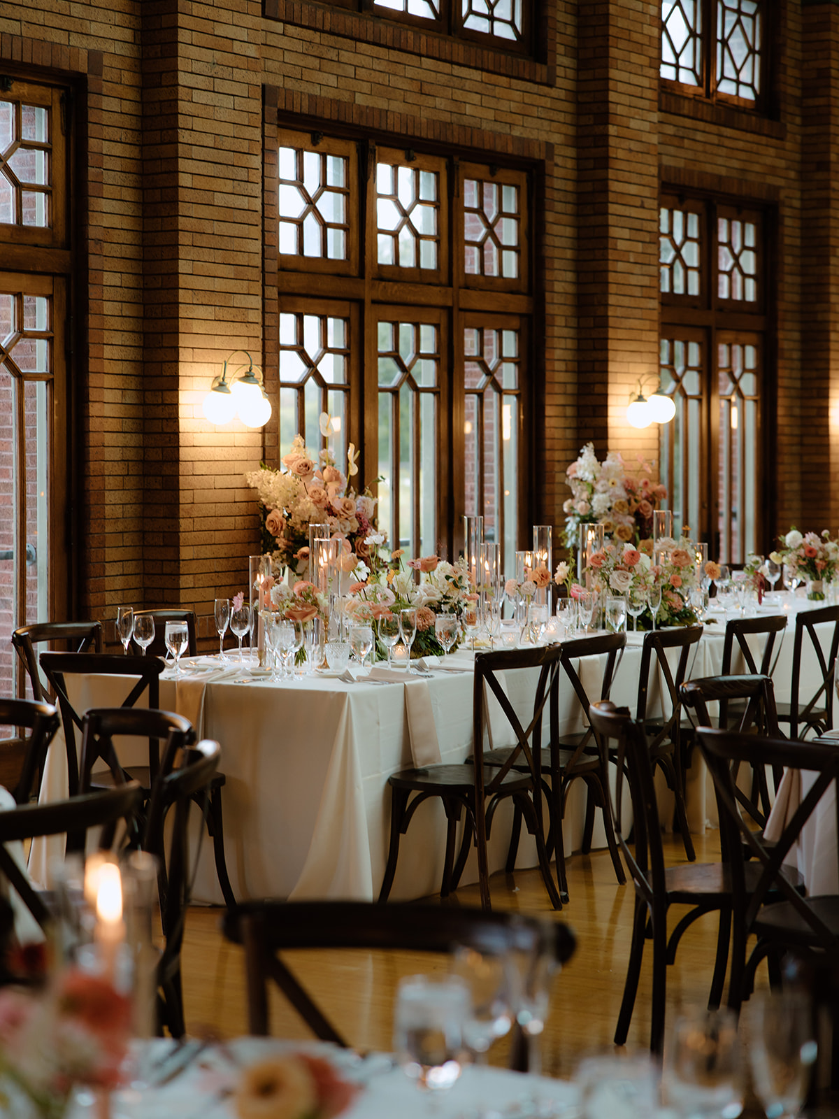 Candlelit wedding tables with peach and blush florals in front of Café Brauer's brick and stained-glass windows