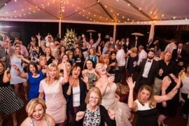 The bride laughing with wedding guests who have their hands in the air on a string-lit reception tent dance floor