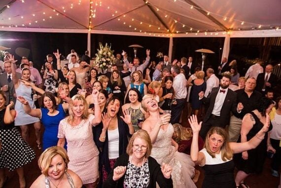 The bride laughing with wedding guests who have their hands in the air on a string-lit reception tent dance floor