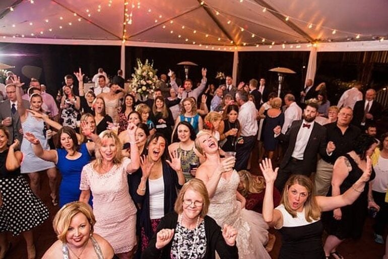 The bride laughing with wedding guests who have their hands in the air on a string-lit reception tent dance floor