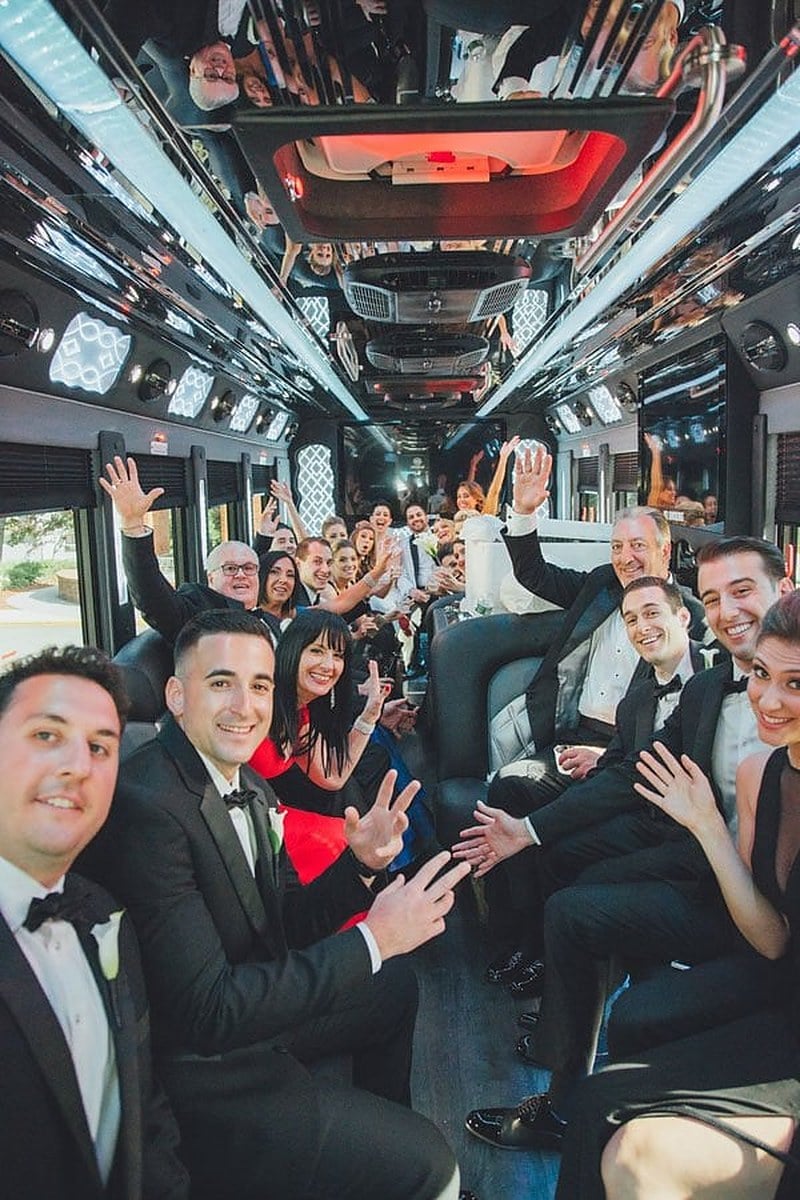 Wedding party and guests waving at the camera inside a party bus